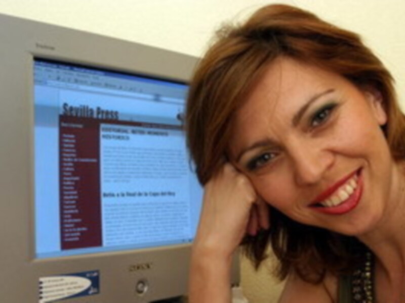 Una mujer sonríe mientras mira una pantalla de computadora con un sitio web en español abierto.