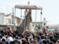 Una multitud de personas participa en una procesión religiosa, con un altar central que sostiene una figura de San Judas Tadeo. El ambiente es festivo y el cielo despejado sugiere un climasoleado.