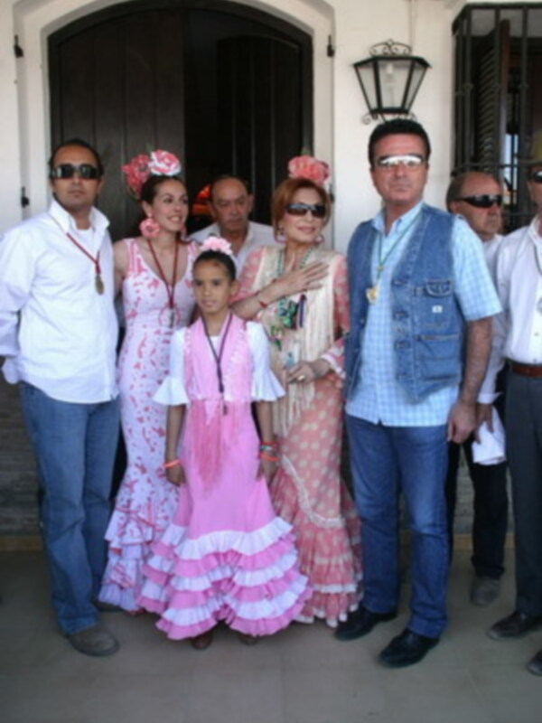 Una familia posa para una foto en la entrada de una casa, todos están vestidos formalmente.