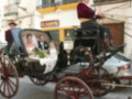 Boda en un elegante coche de caballos, con novia y novio sonrientes, en una calle con edificios blancos y amarillos.