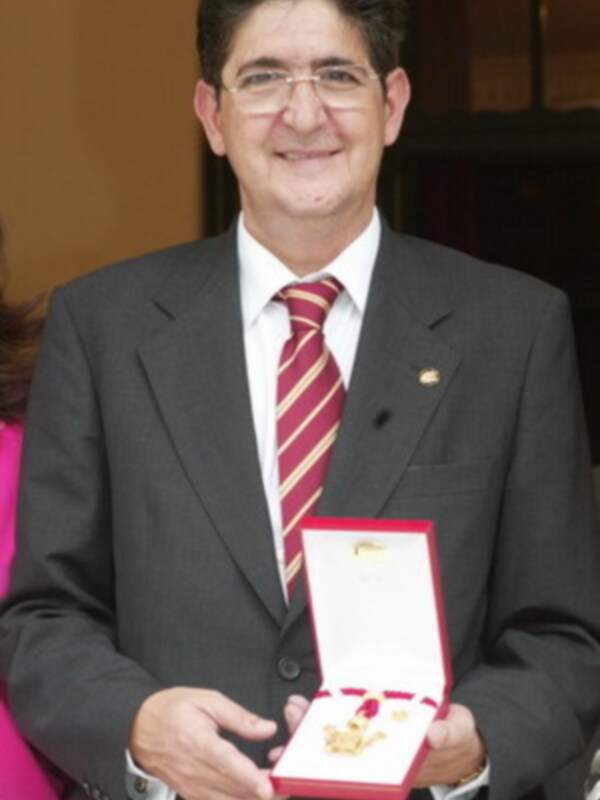 Persona en traje con medalla en caja roja, posando con sonrisa en un evento formal.