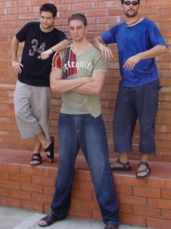 Tres jóvenes posando juntos contra un muro de ladrillo rojo.