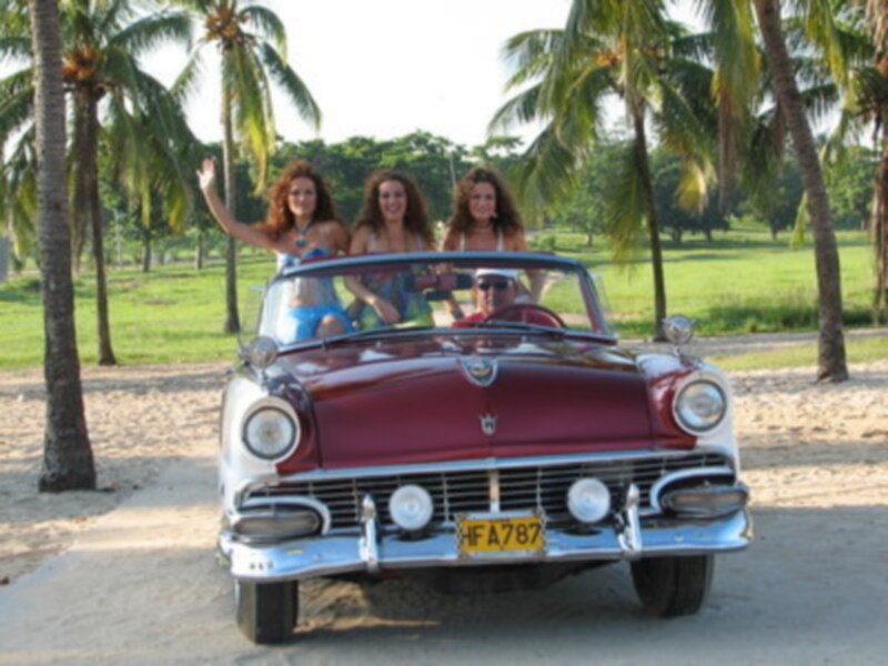 Tres mujeres disfrutan de una tarde relajada en una clásica carrocería americana en una playa tropical.