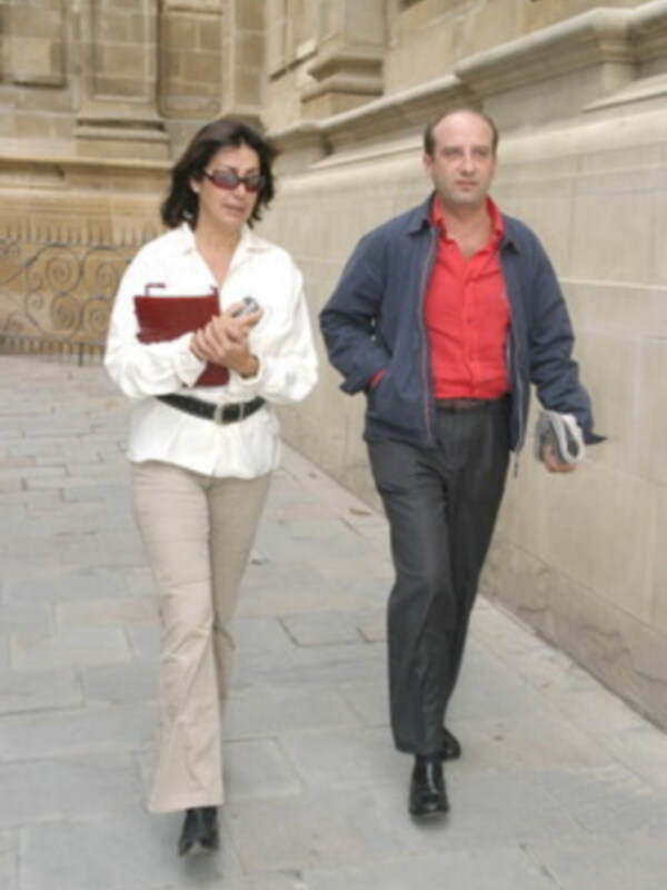 Una pareja caminando juntos, la mujer lleva un bolso rojo y el hombre un bolso blanco, ambos están usando pantalones y camisas de colores diferentes.