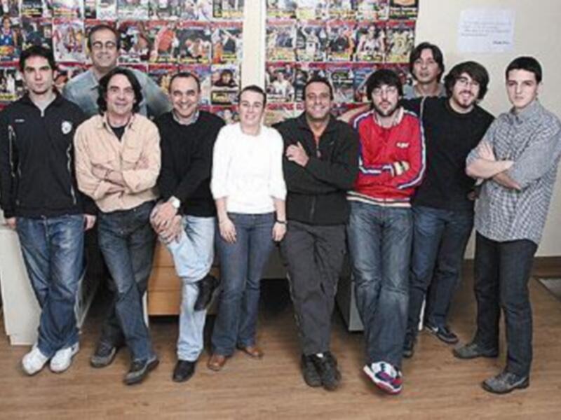 Un grupo de personas posando juntos en un ambiente vibrante, posiblemente un estudio o sala de reuniones, rodeados de carteles y decoración.