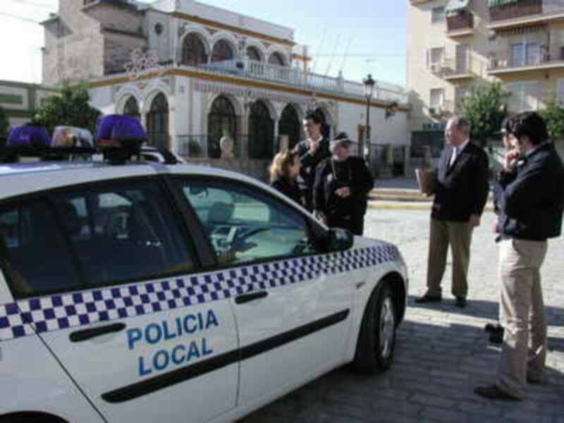 Vehículo de Policía Local en una plaza con personas reunidas, edificios históricos al fondo.