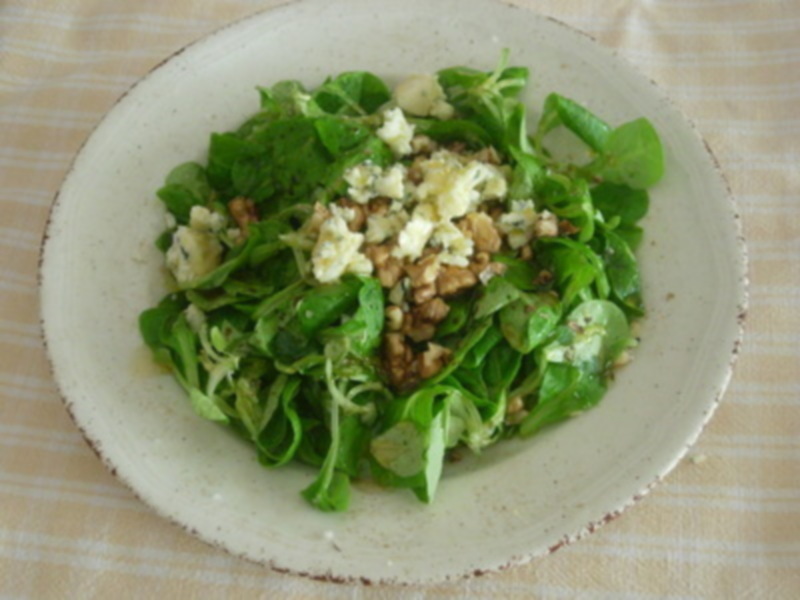 Un delicioso ensalada de hojas verdes con queso azul y nueces en un plato blanco sobre una mantequilla de color crema.