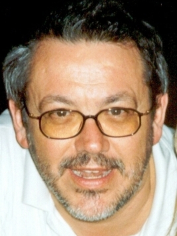 Retrato de hombre con barba y gafas, sonriendo en una foto de estudio.