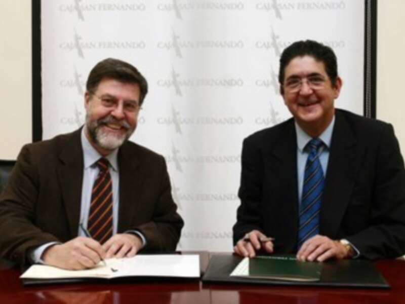 Dos hombres en traje firmando documentos en una oficina formal.