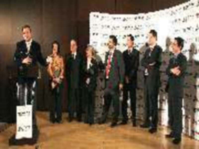 Premios de la industria cinematográfica con participantes en trajes formales en un escenario con carteles de premios.