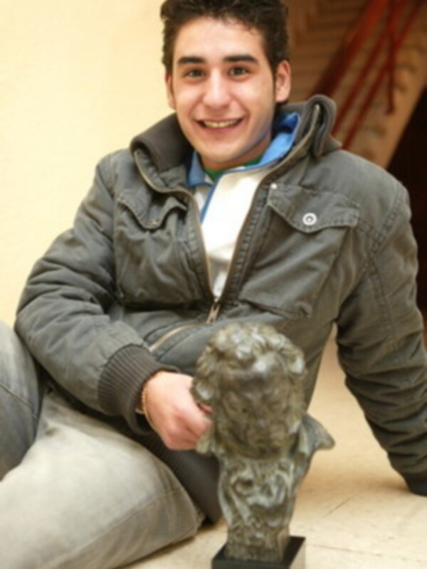 Un joven sonriendo mientras sostiene una estatua de bronce.