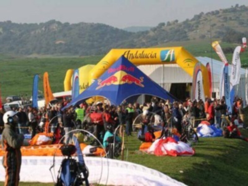 Un evento deportivo con personas en el campo, banderas y estructuras inflables en el fondo.