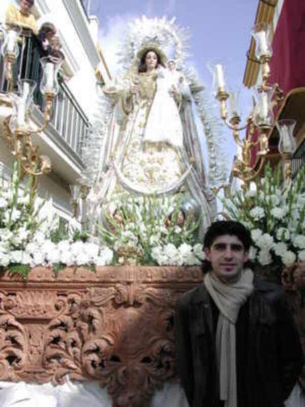 Festividad religiosa con imagen procesional de la Virgen y hombre en primer plano.