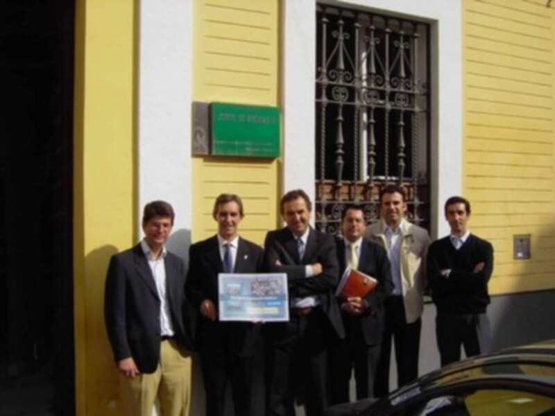 Equipo de negocios posando con un certificado frente a una fachada amarilla.