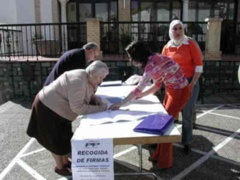 Personas recogiendo firmas en una mesa con un cartel que dice 'Recogida de firmas'.