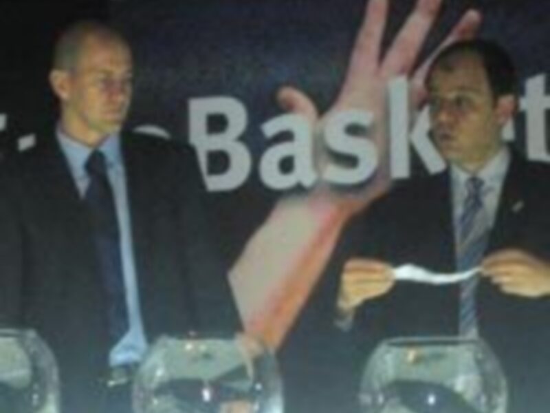 Dos hombres en una presentación de baloncesto, uno sosteniendo un papel.