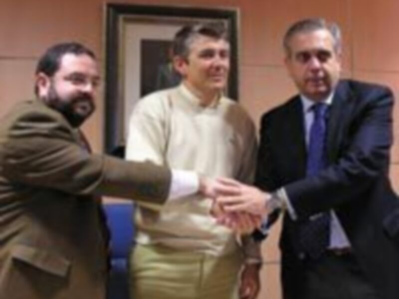 Tres hombres intercambian un apretón de manos en una reunión formal, con un fondo de paredes beige y una puerta de madera.