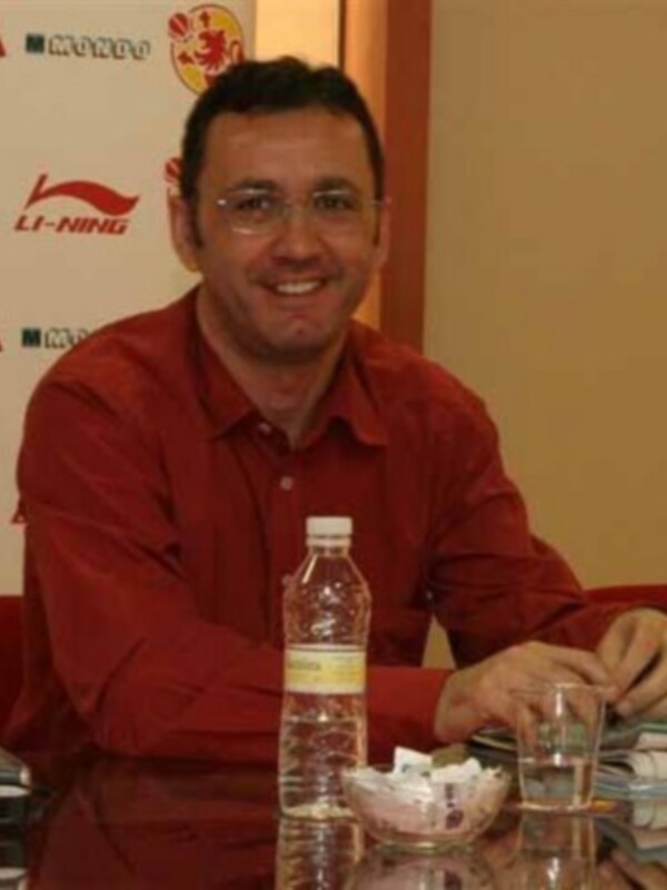 Persona sonriente en una reunión, sentado en una mesa con agua y documentos.