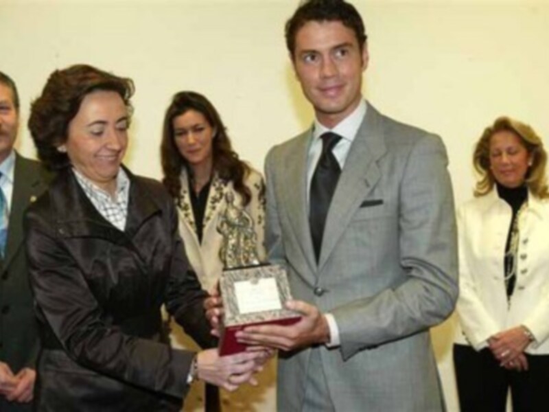 Persona en traje gris recibe un premio de manos de otra mujer, rodeada por espectadores en un evento formal.