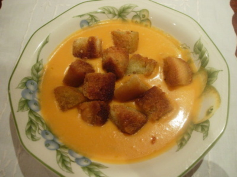 Un plato de crema de calabaza con croutons dorados en la parte superior. La crema tiene un color dorado amarillento y está servida en una porción de plato con bordes verdes y azules.