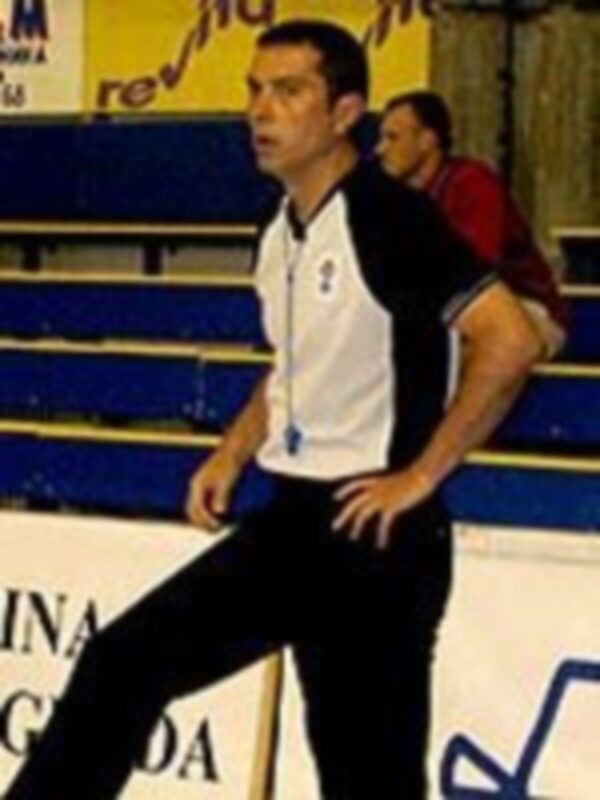 Un hombre en una cancha de baloncesto, posando con una camiseta blanca y azul, en un entorno deportivo.