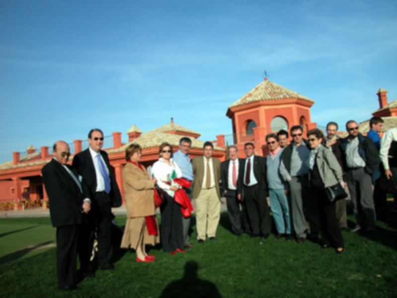 Una imagen de un grupo de personas posando en un campo de golf con un edificio de estilo colonial en el fondo.
