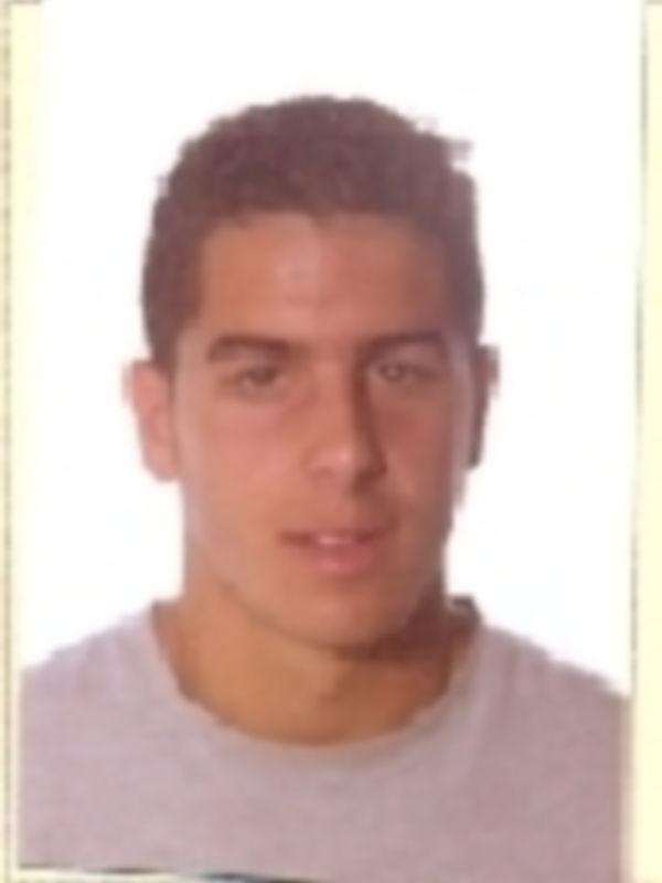 Retrato de hombre joven con cabello oscuro y camiseta gris, frente a fondo blanco.