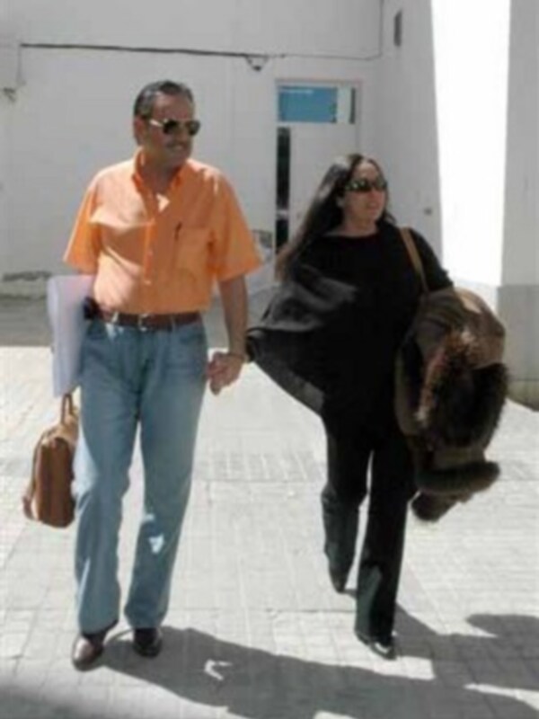 Un hombre y una mujer caminan juntos por un patio, el hombre lleva una carpeta y ambos parecen estar en un entorno urbano.