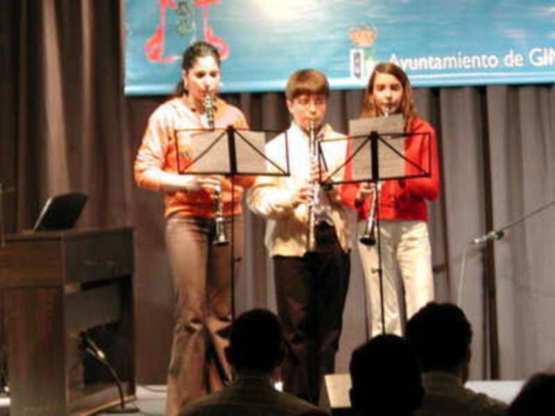 Tres jóvenes músicos tocando flautas en un escenario con el Ayuntamiento de Gijón en el fondo.