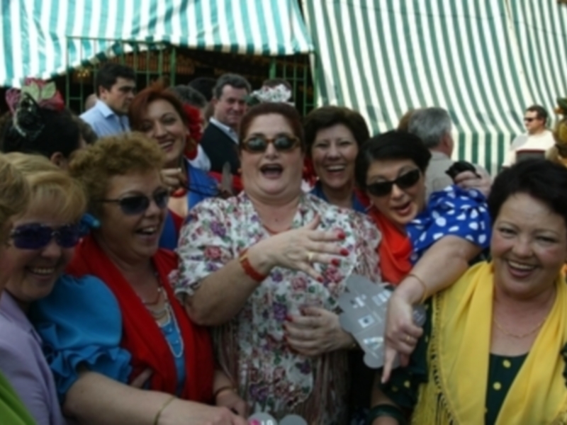 Una multitud de personas riendo y disfrutando en un evento al aire libre, con una tenda de tela en el fondo.