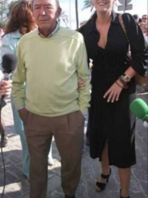 Entrevista en una plaza pública con un hombre y una mujer, rodeados de personas y palmeras en el fondo.