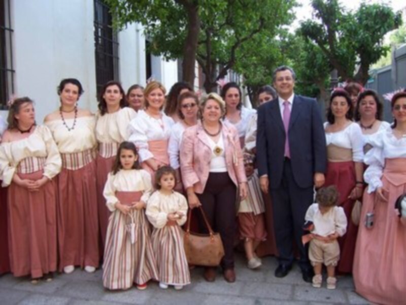 Una familia posando para una foto en trajes tradicionales, con mujeres en vestidos largos y hombres en trajes formales. El ambiente es festivo y la celebración parece ser importante.