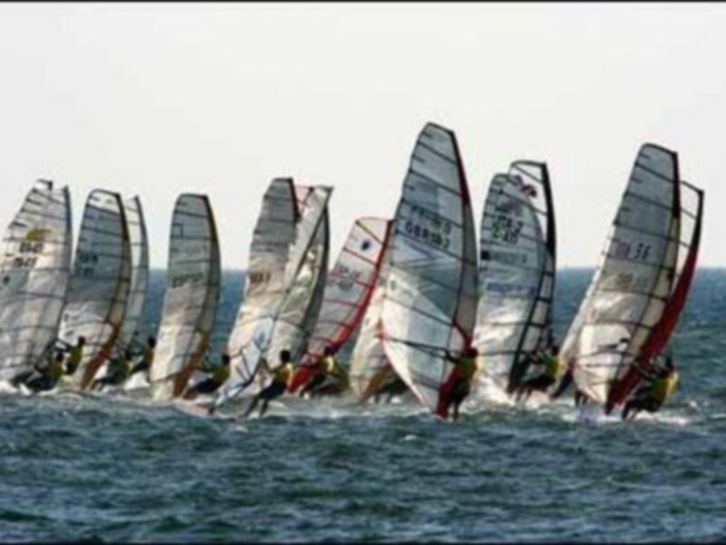 Competición de vela de viento en el mar con veleros navegando juntos.