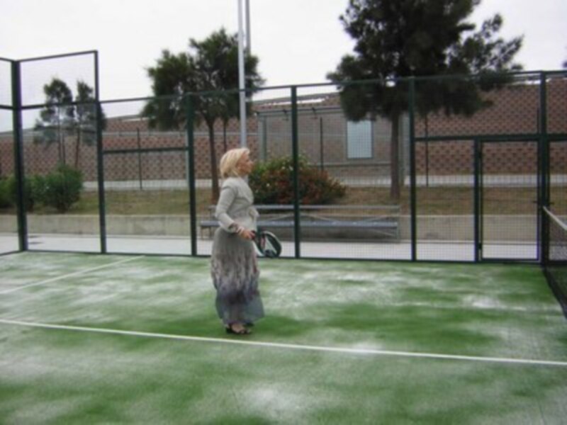 Una persona disfruta del tiempo libre en una cancha de pádel, rodeada de una cerca y árboles.