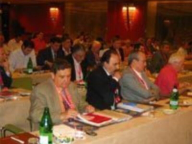 Asistentes participando en una reunión en un ambiente formal con mesas llenas de documentos y bebidas.