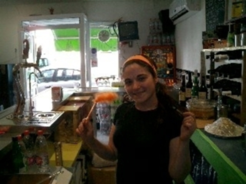 A una persona sonriendo mientras sostiene un limón y una cuchara. La escena parece ser en un área de cocina con varios elementos como un descompresor, una caja de madera y un mostrador.