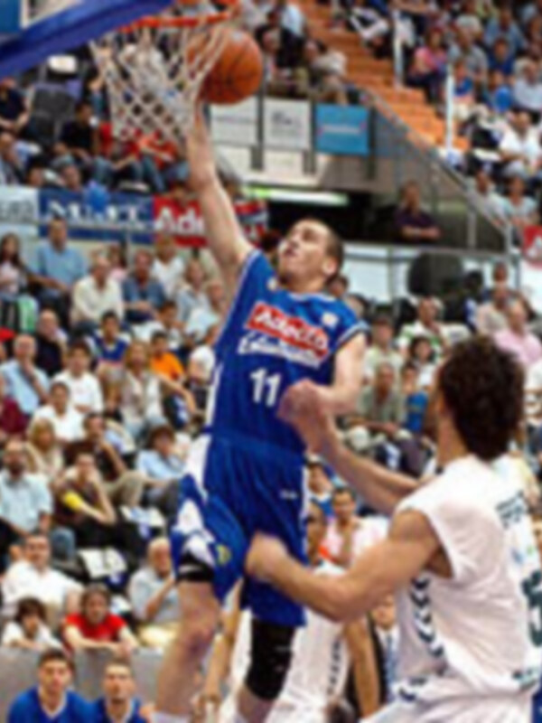 Jugador en acción durante un partido de baloncesto, realizando un mateso con el balón en la canasta.