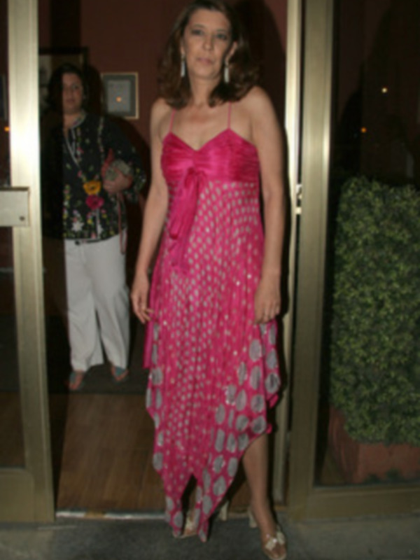 Una mujer vestida con un vestido de color rosa y blanco con un diseño de corazones, posando en una entrada de edificio. La imagen muestra detalles de su vestido y su expresión facial.