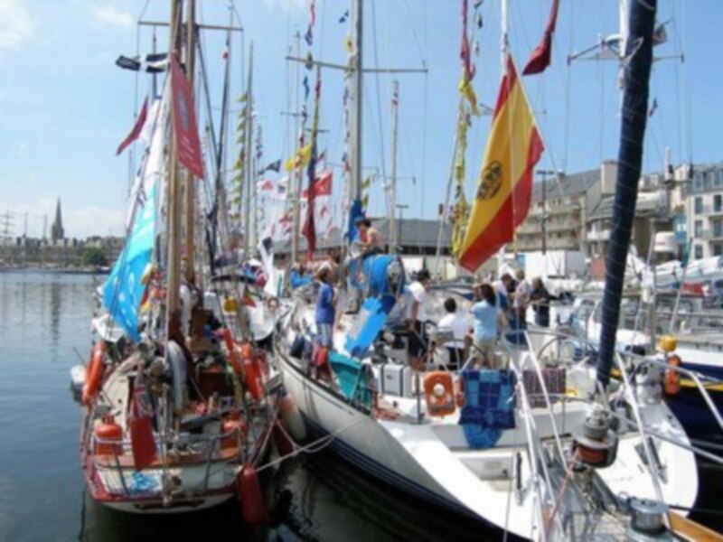 Barcos de vela amarrados en un puerto con banderas y gente en la cubierta.