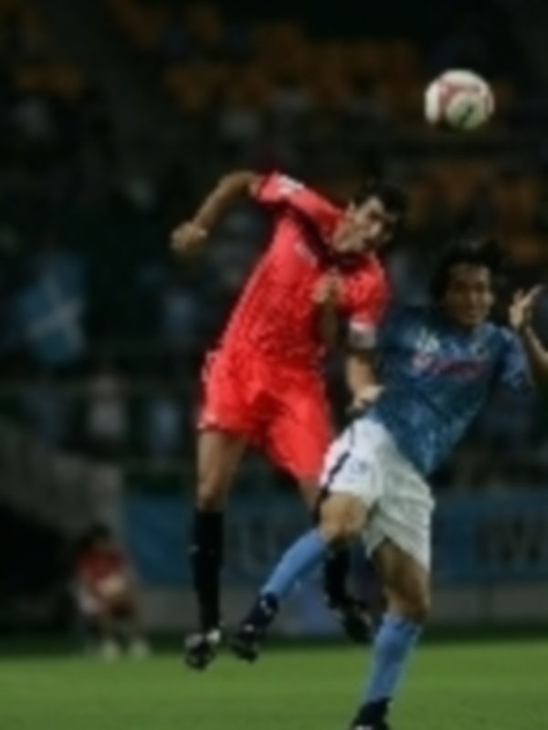 Un jugador de fútbol en acción durante un partido, con un rival en el fondo.