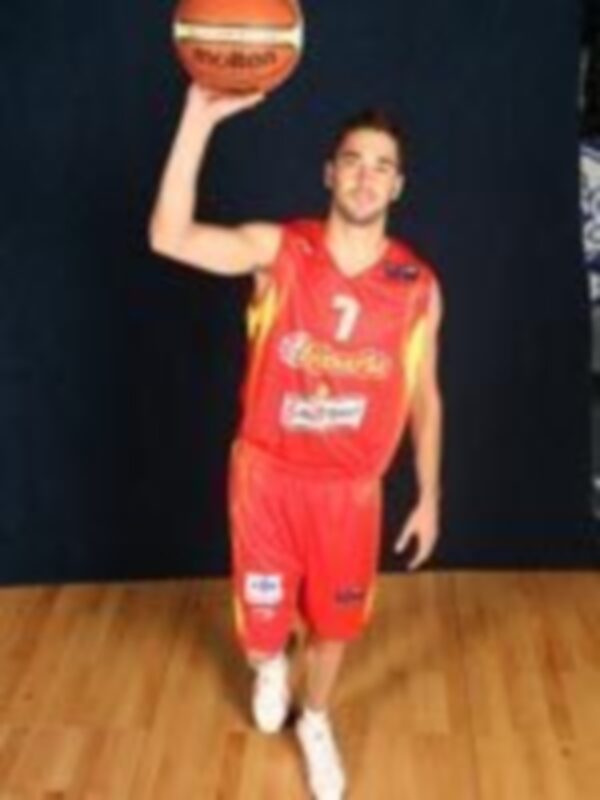 Jugador de baloncesto en uniforme rojo con el número 7, sosteniendo un balón de baloncesto en un entorno deportivo.