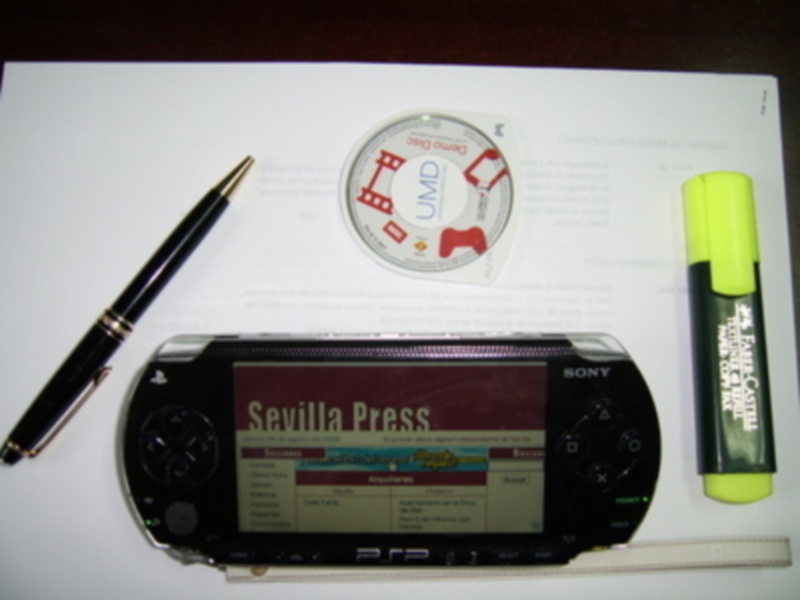 Consola Sony PSP con pantalla 'Sevilla Press' y accesorios de escritorio.