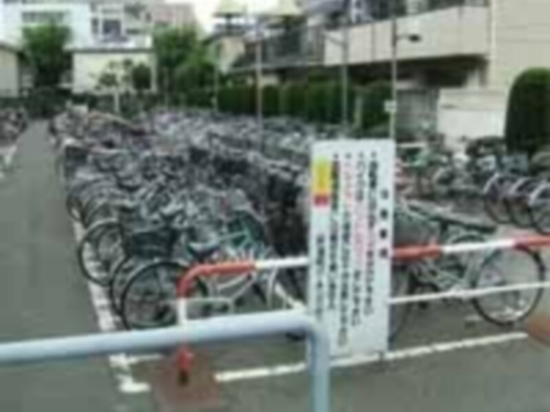 Un estacionamiento de bicicletas en Japón, con numerosas bicicletas apiladas en filas y un cartel informativo en el fondo.