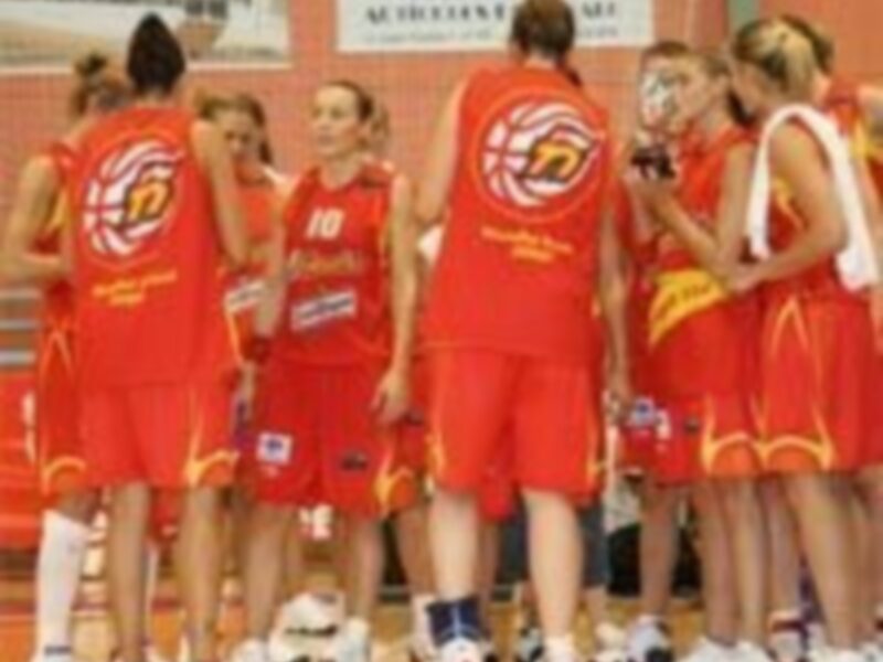 Equipo de baloncesto en uniforme rojo celebrando en el banquillo tras un partido.