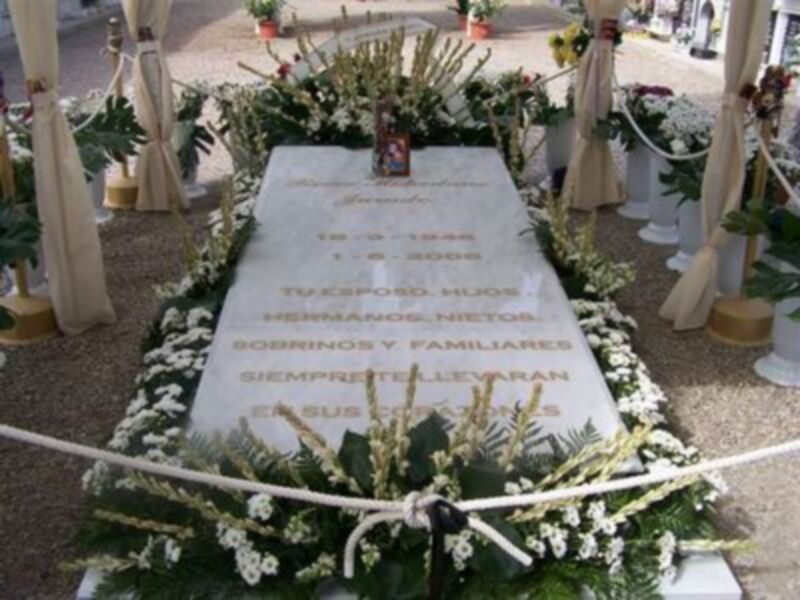 Tumba conmemorativa adornada con flores y velas, dedicada a un ser querido fallecido en 2006.