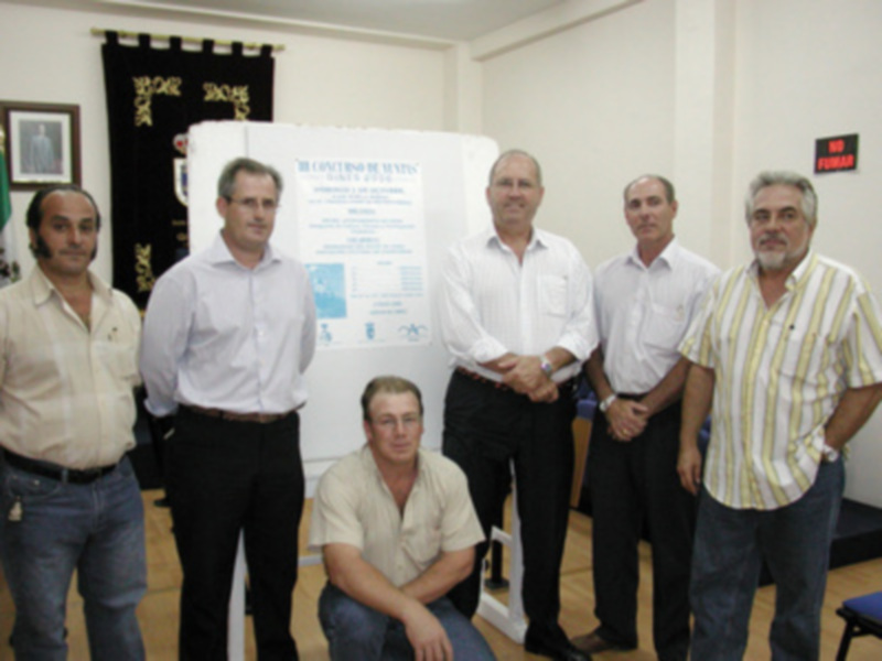 Grupo de hombres posando junto a un cartel informativo en una sala.