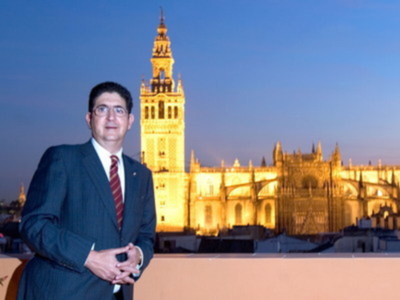 Hombre en traje frente a la Catedral de Sevilla y la Giralda al atardecer.
