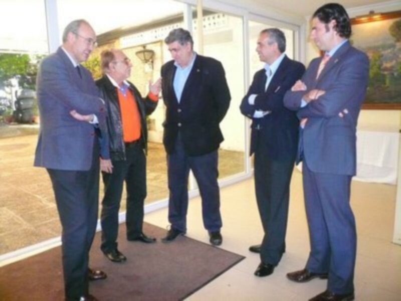 Un grupo de hombres en trajes y camisas de negocios están discutiendo en un entorno de oficina con ventanas y una alfombra marrón.