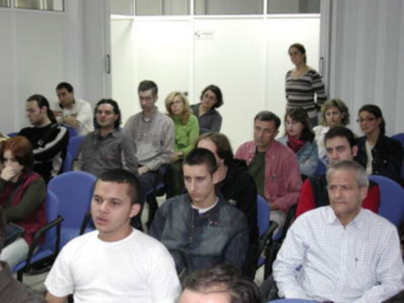Una reunión de trabajo en un espacio de oficinas, con personas sentadas en filas, mirando hacia la pantalla.