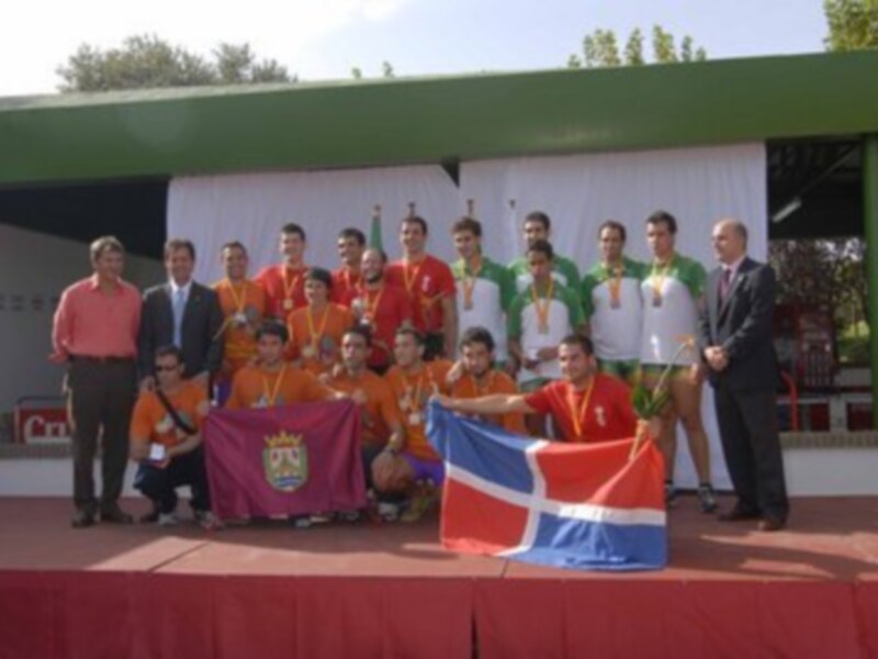 Equipo deportivo con medallas posa en un escenario con bandera y escudo regional, celebrando un logro.